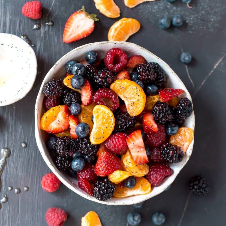 over head photo of berry fruit salad with berries and orange segments on black background