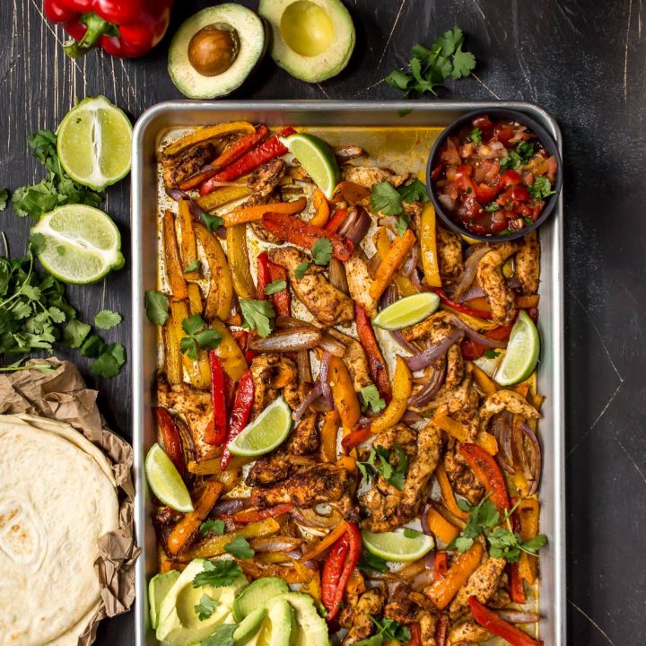 overhead photo of chicken, bell peppers and limes in sheet pan. Tortillas, limes and avocados on the side for chicken fajitas