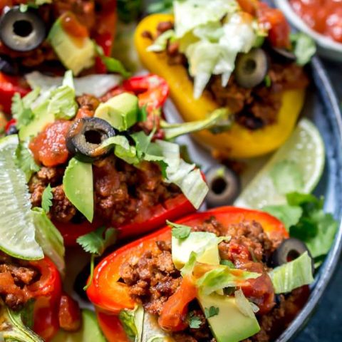 close up of stuffed peppers topped with lettuce, avocado, olives and cilantro.