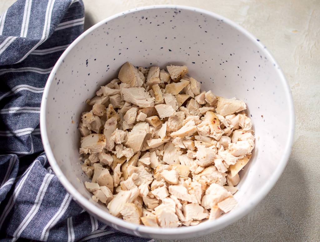 baked chicken breast that is chopped and in a white bowl with blue flecks