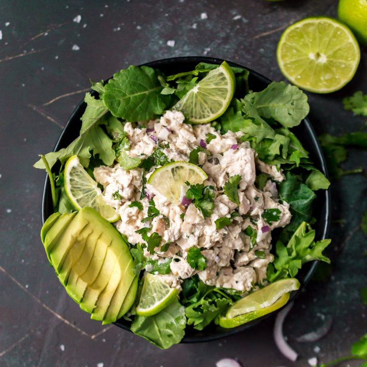 over head photo of cilantro lime chicken, sliced avocado in black bowl on black background, limes on the side