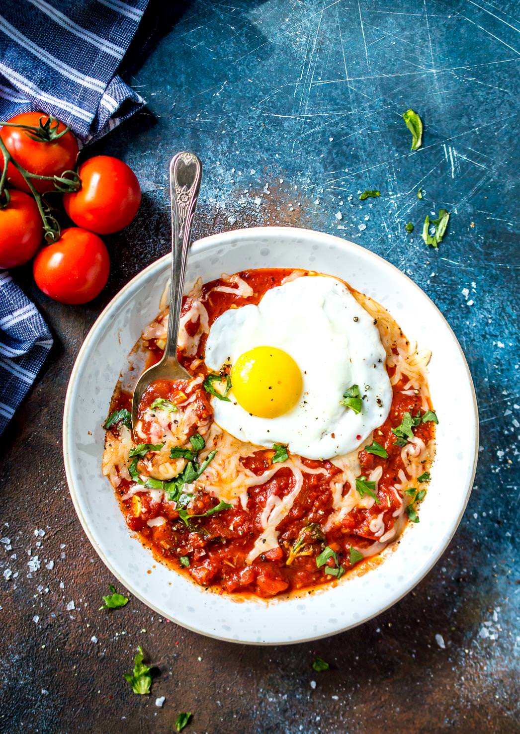 overhead view of white bowl filled with fried egg in purgatory, vine tomatoes on the side