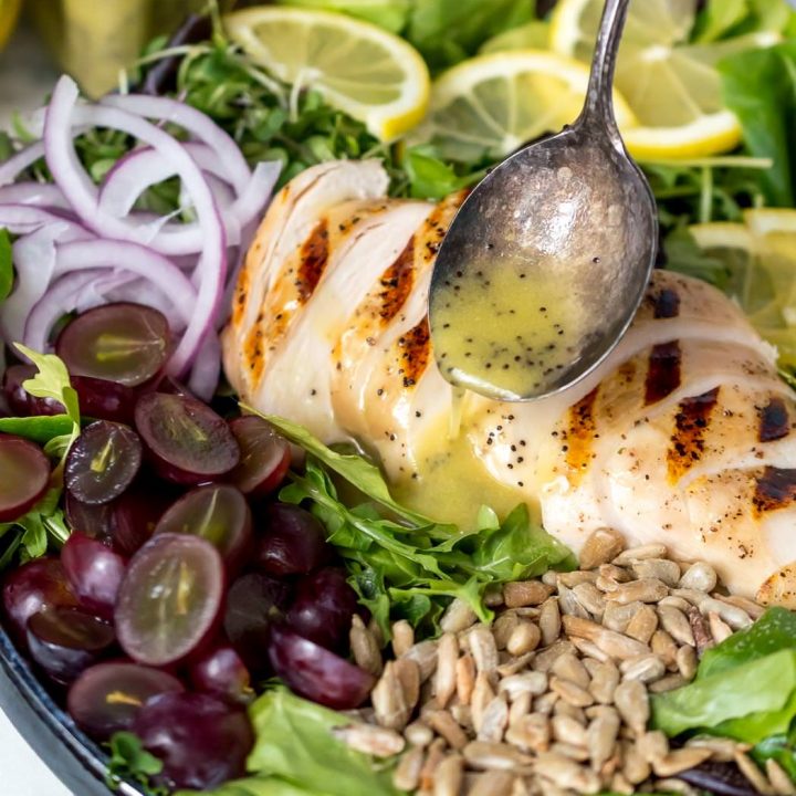 spoon drizzling lemon poppy seed dressing over grilled chicken salad