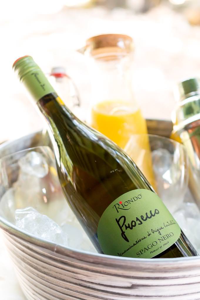 phot of prosecco bottle in bucket of ice. orange juice in the background