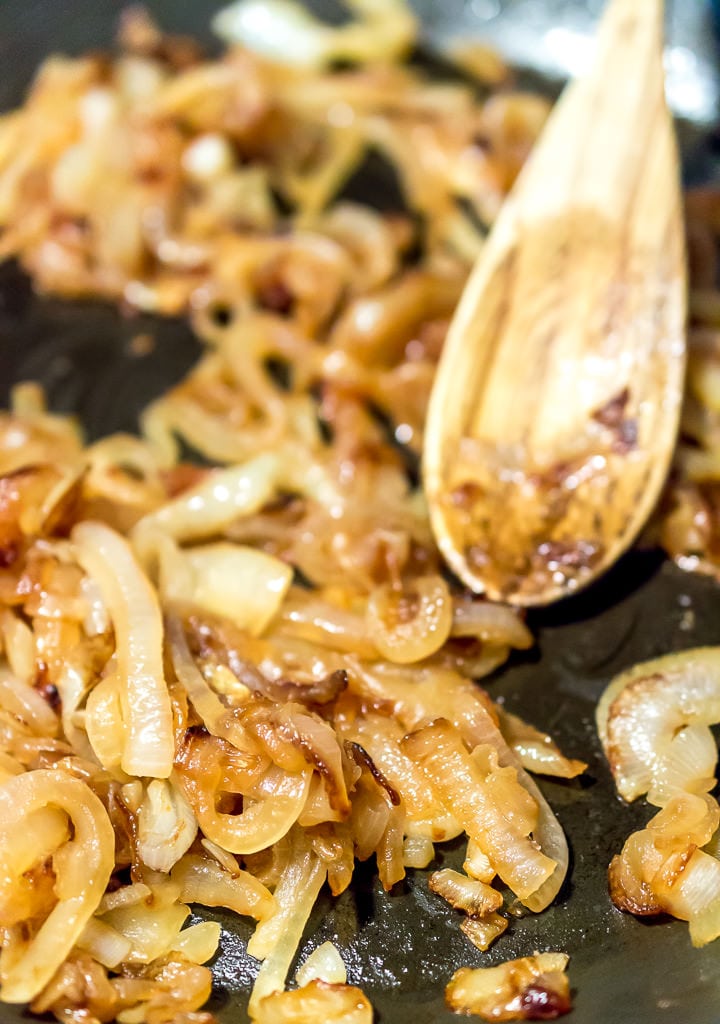 caramelized onions in saute pan being stirred with wooden spoon