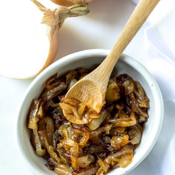 white bowl filled with caramelized onions and a mini bamboo serving spoon