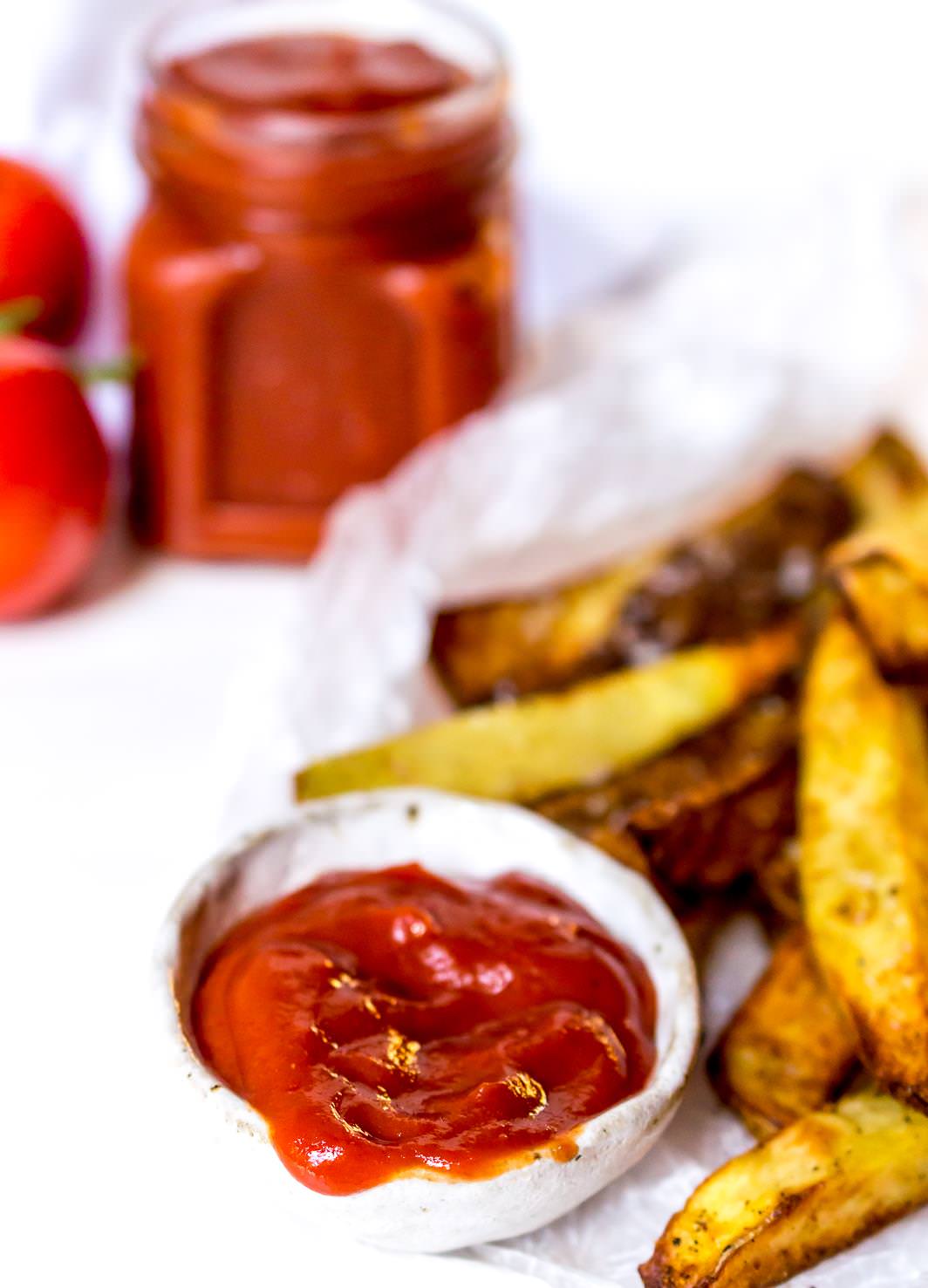 bright red ketchup in small white bowl next to oven fries