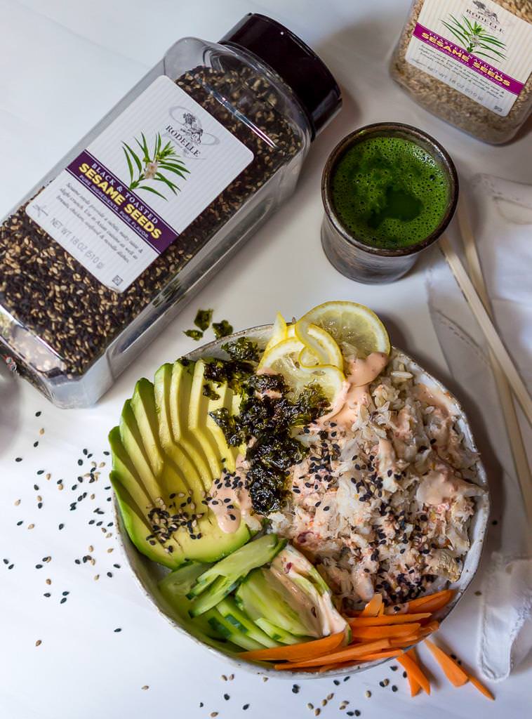 spicy crab sushi bowl next to bottle of black sesame seeds and a cup of green tea