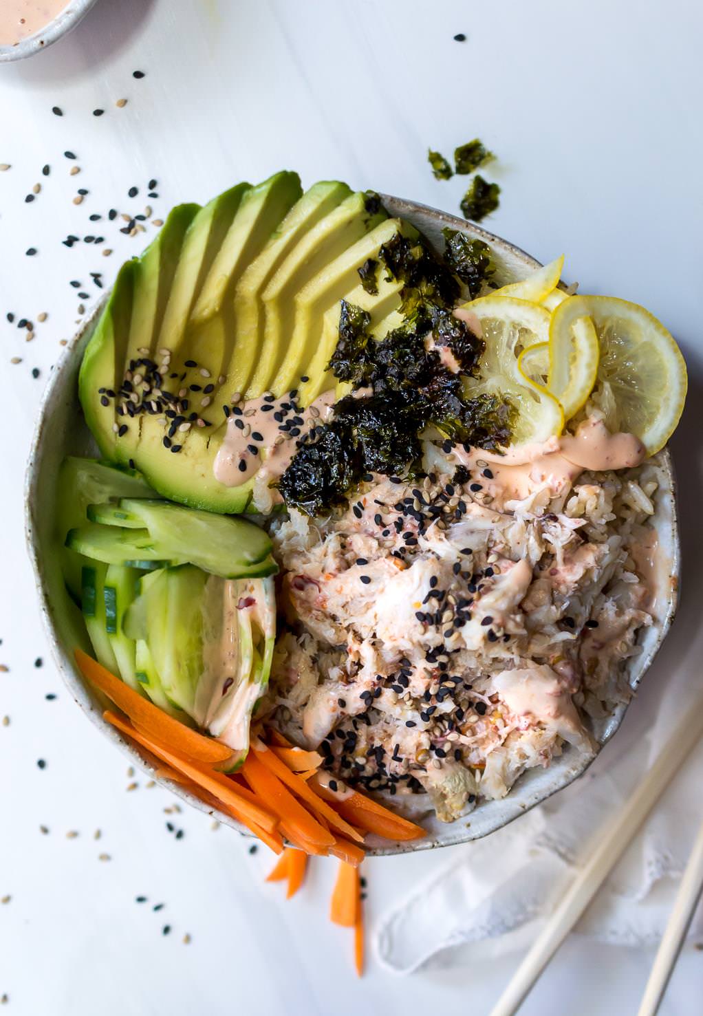 over head photo of sushi bowl filled with avocado, cucumber, carrots, lemon, crab and seaweed