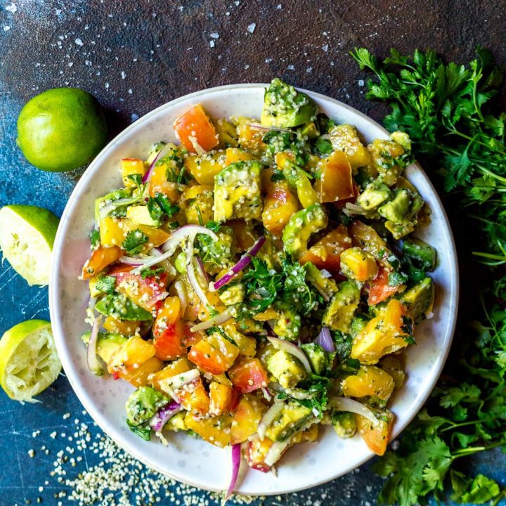over head photo of white bowl filled with avocado tomato salad on a blue and brown background
