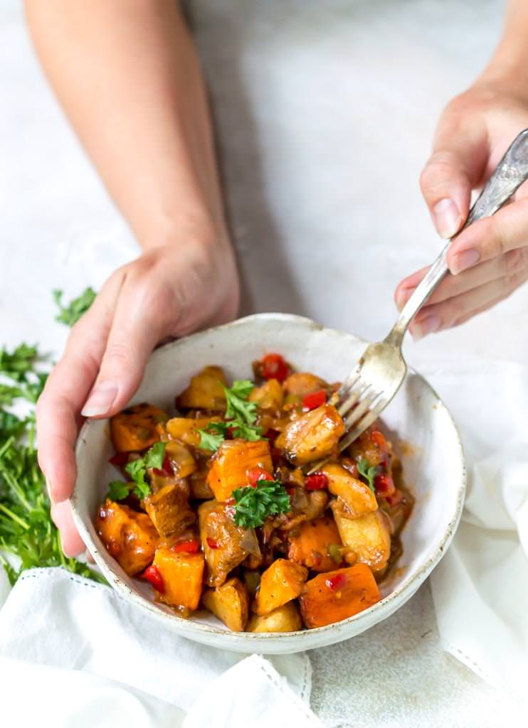 hand holding white bowl and fork scooping a bite of an easy weeknight dinner, chipotle chicken vegetable hash