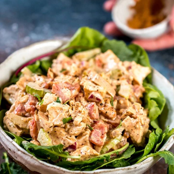 a bowl full of jamaican jerk chicken salad with jerk seasoning in the background