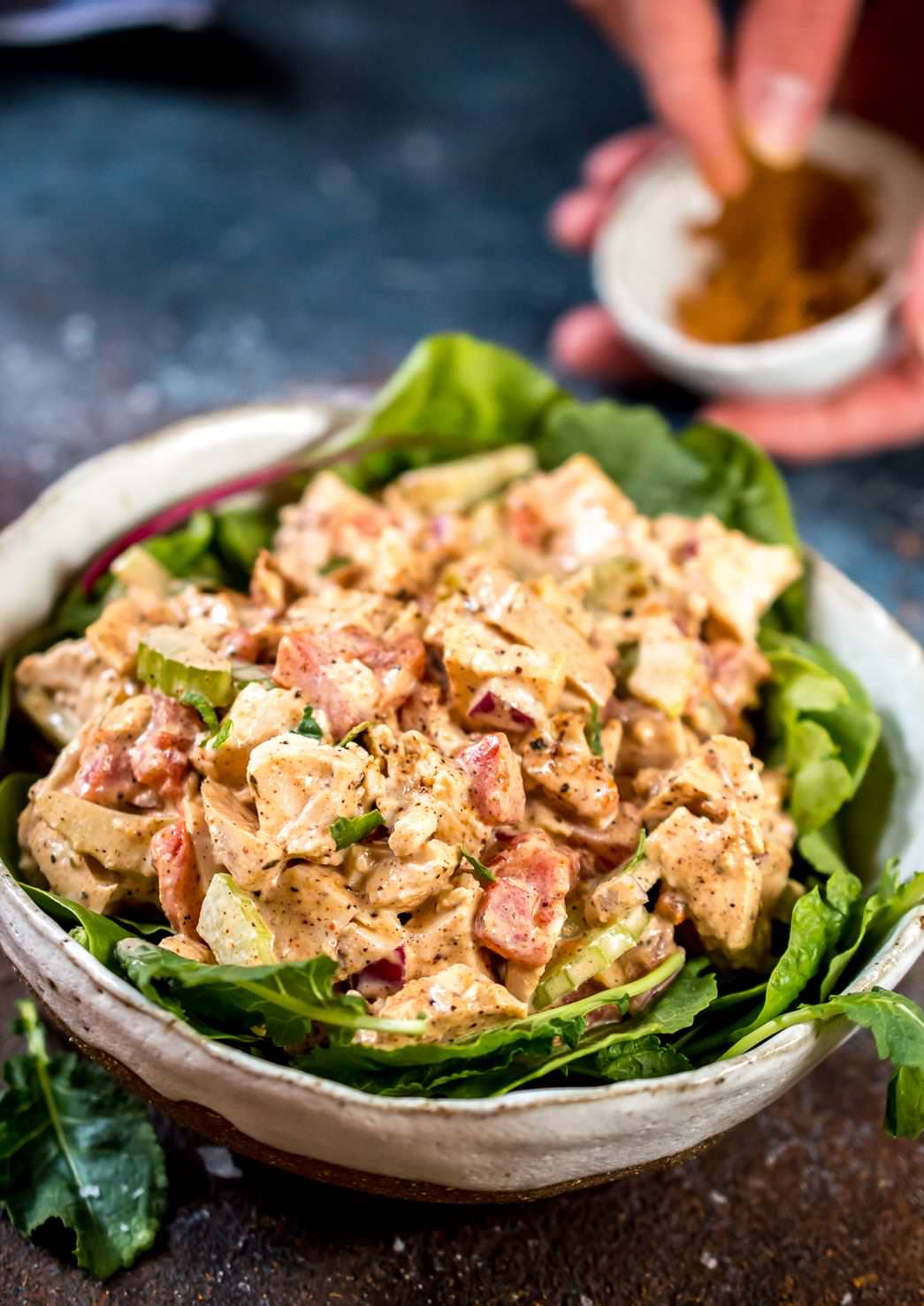 a bowl full of jamaican jerk chicken salad with jerk seasoning in the background