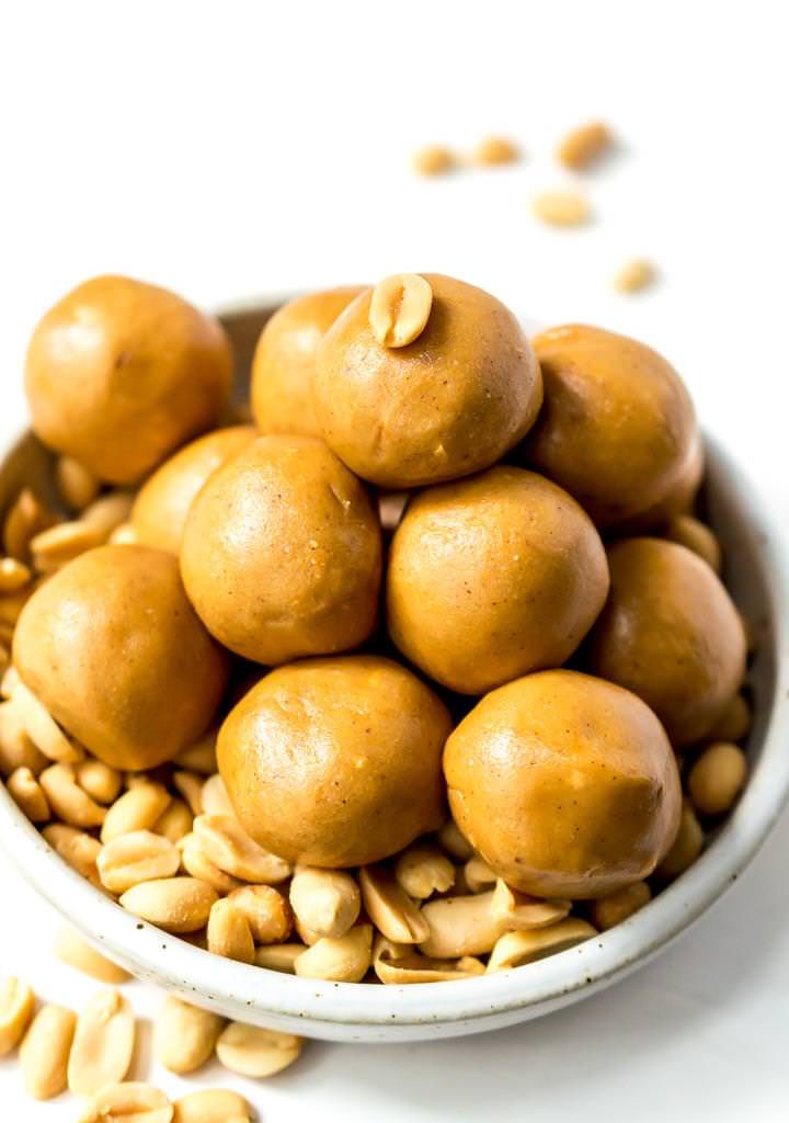 close up photo of peanut butter protein balls in white bowl filled with shelled peanuts