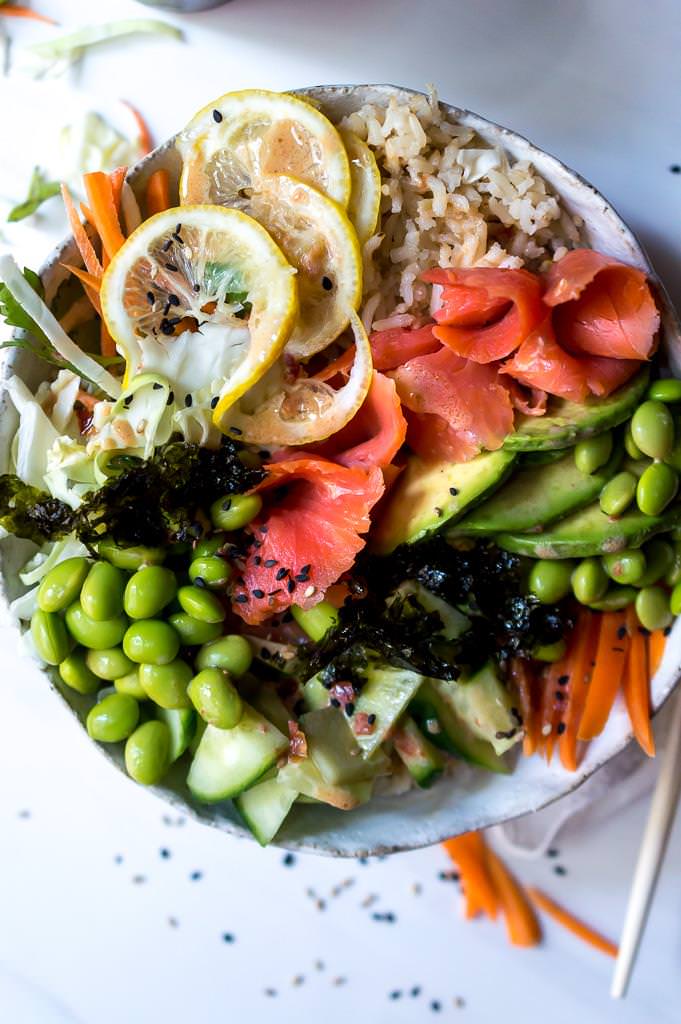 close up photo of salmon sushi bowl filled with rice, salmon, lemon, soy beans and cucumbers