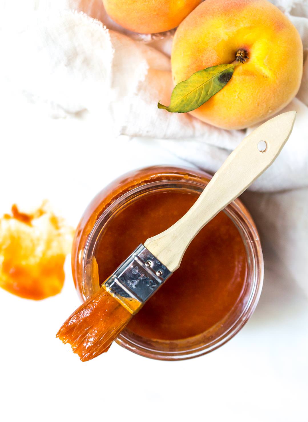over head photo of peach barbecue sauce recipe in glass jar with bbq brush on top
