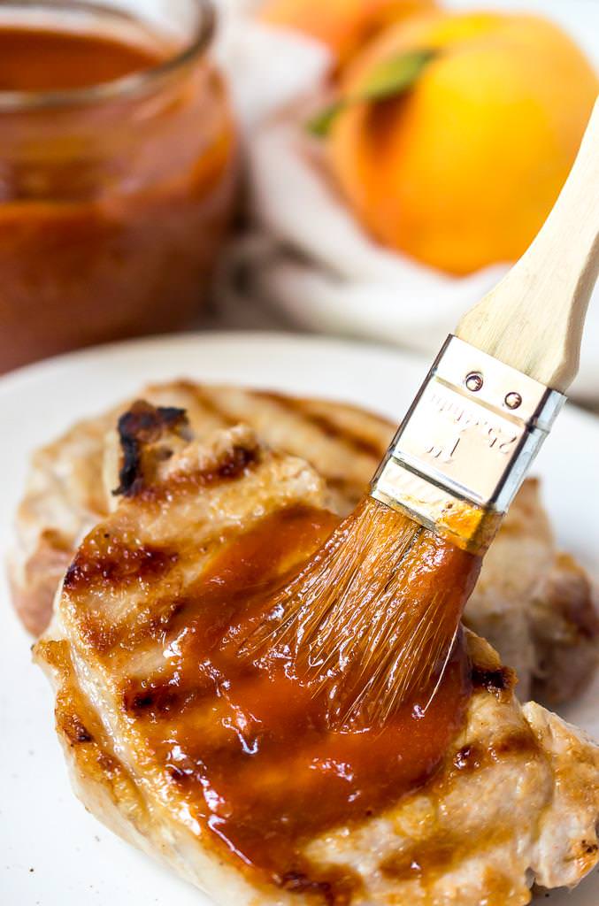 bbq brush slathering peach barbecue sauce onto a grilled pork chop