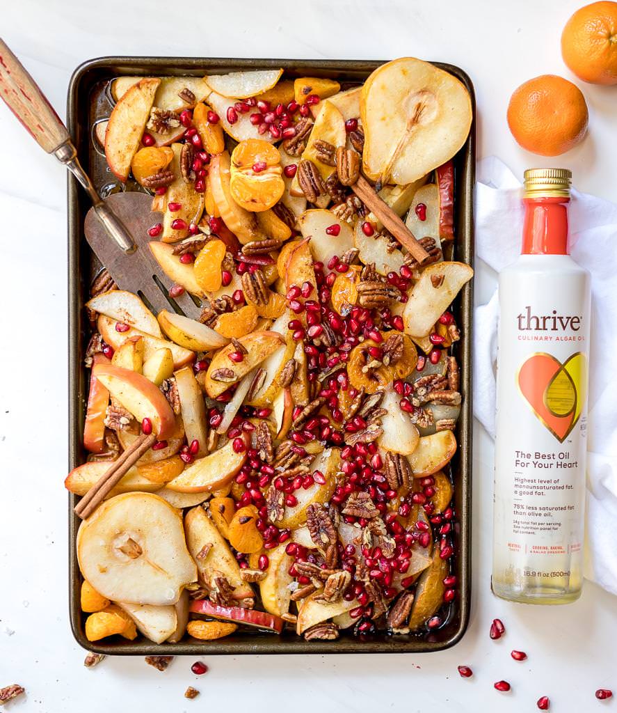 baking sheet with baked apples, pears and mandarins with a bottle of thrive oil on the side