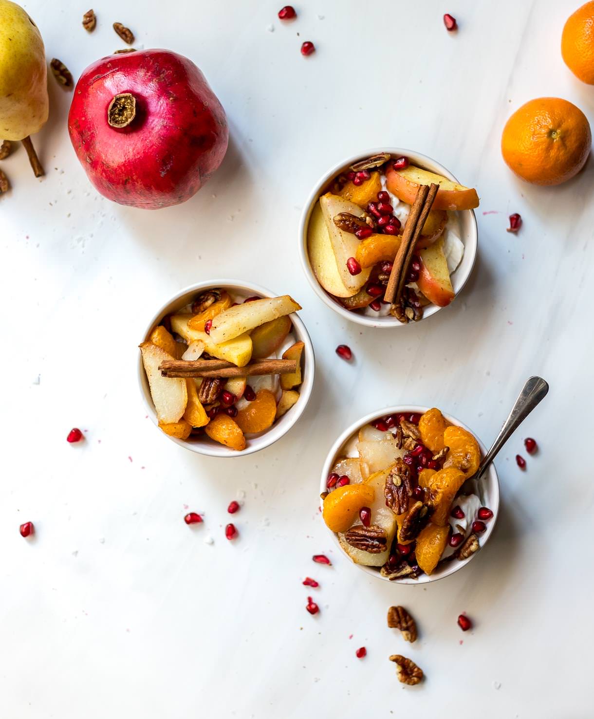 three small bowls of yogurt topped with baked apples, pears and mandarins