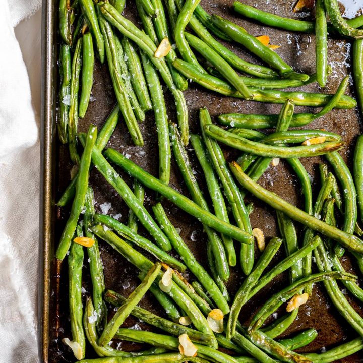 roasted fresh green beans with slices of golden garlic in a dark metal baking sheet