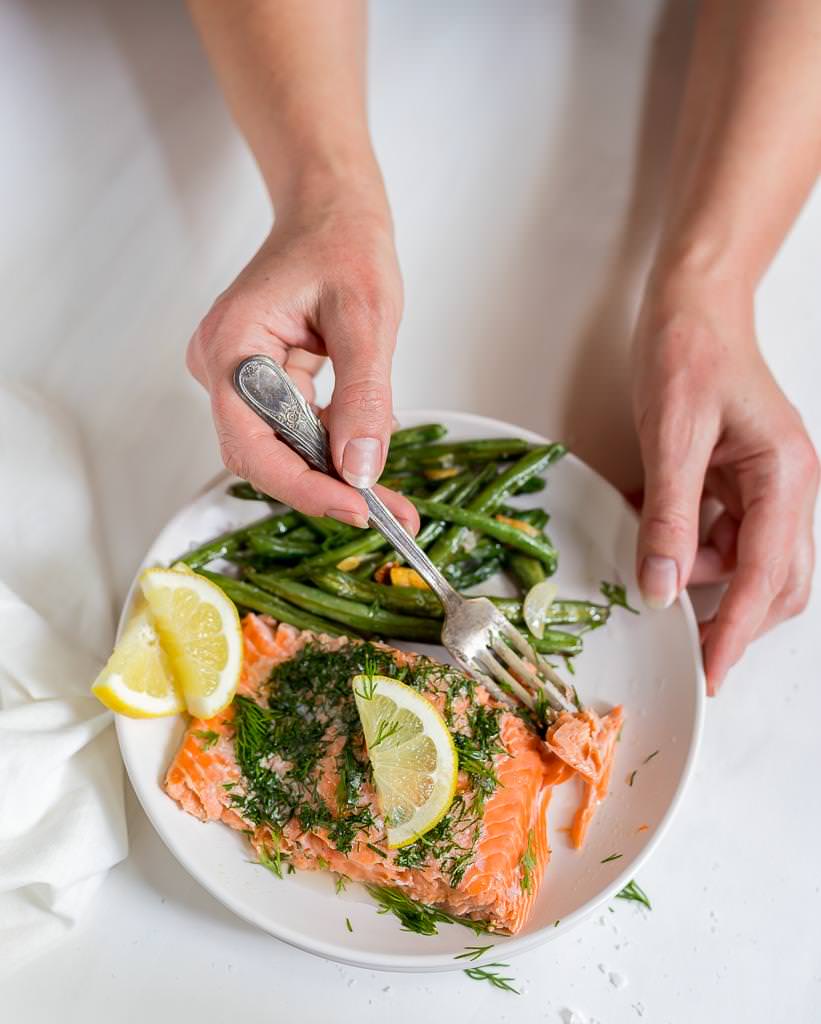 white plate with fresh baked salmon, green beans and lemons