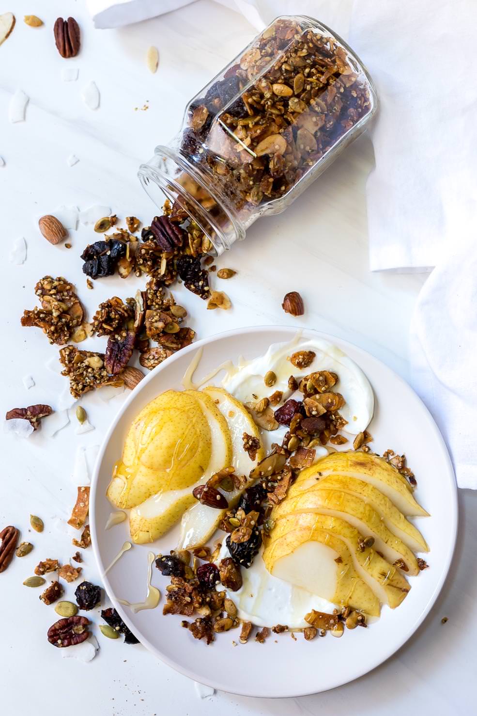 sliced pears and yogurt topped with paleo granola and a jar of granola on the side