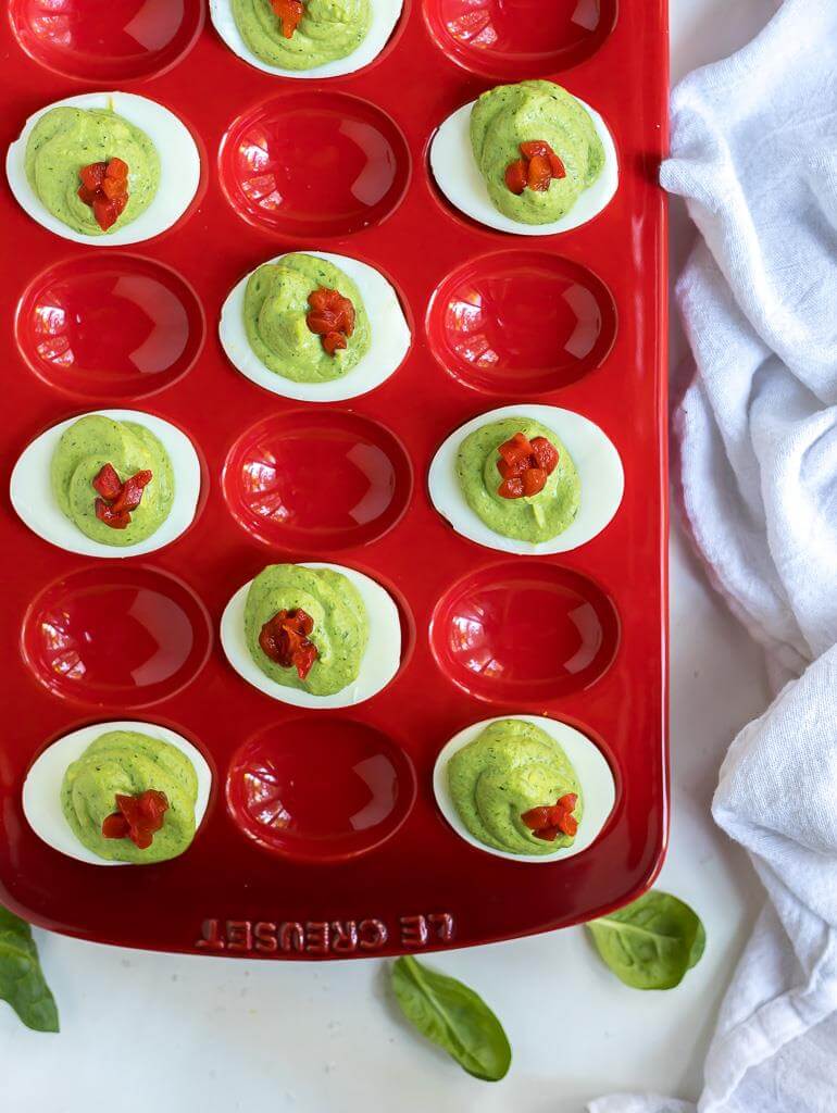 green and red spinach deviled eggs in red serving platter