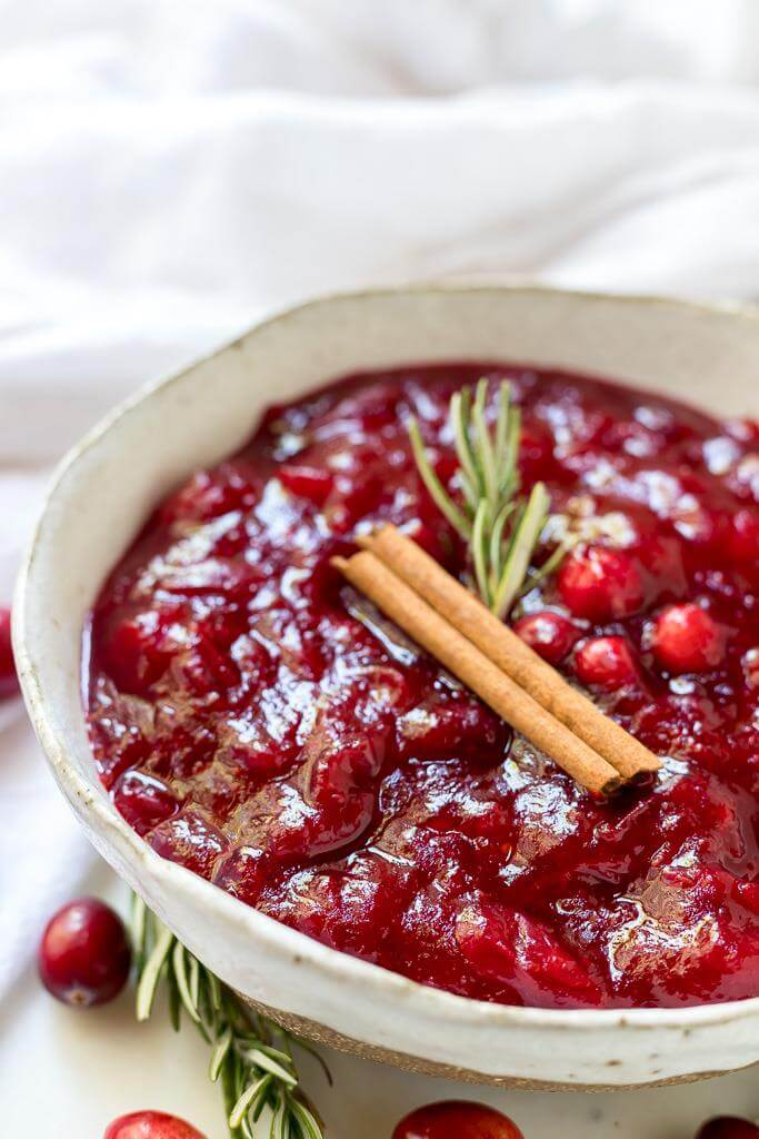 homemade paleo cranberry sauce topped with a cinnamon stick and rosemary sprig