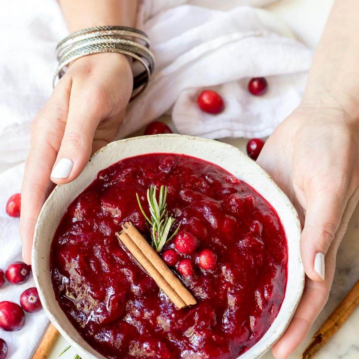 hands holding a white bowl filled with homemade paleo cranberry sauce