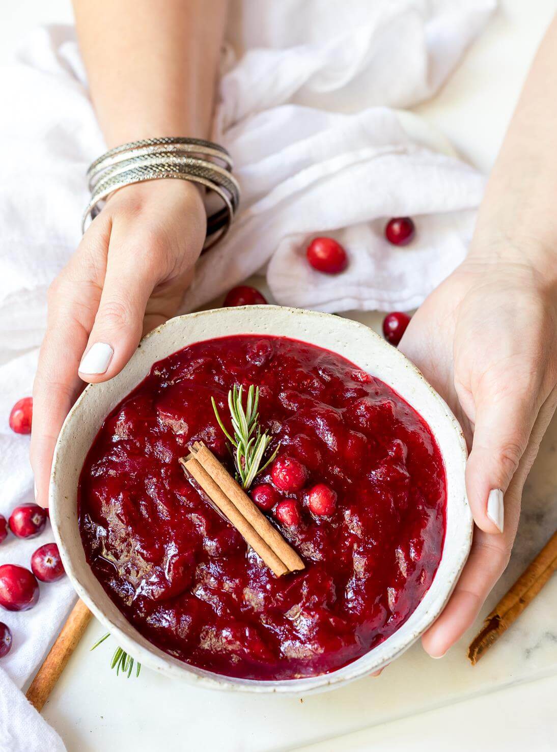 hands holding a white bowl filled with homemade paleo cranberry sauce