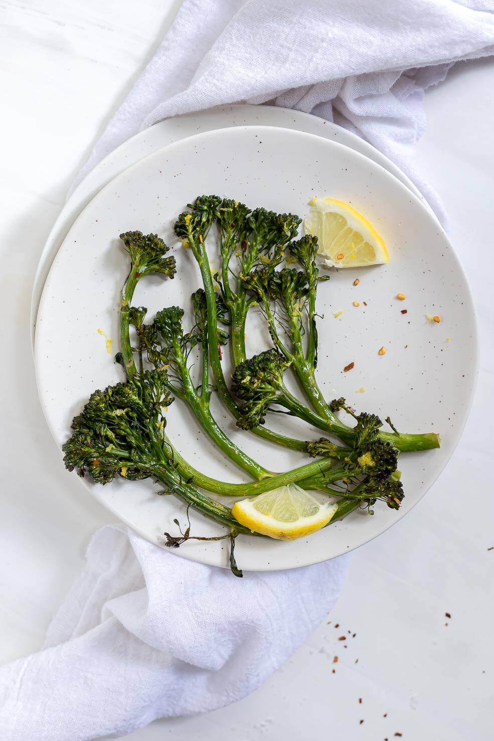 white plate with fresh green roasted broccolini and lemons