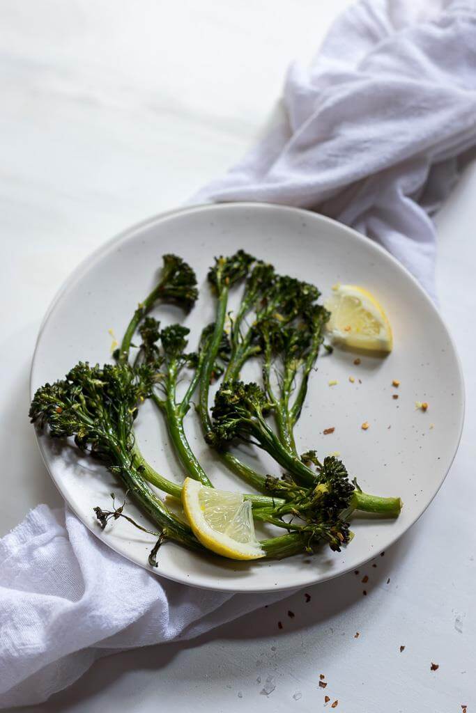 finished roasted broccolini recipe on white plate with lemon wedges