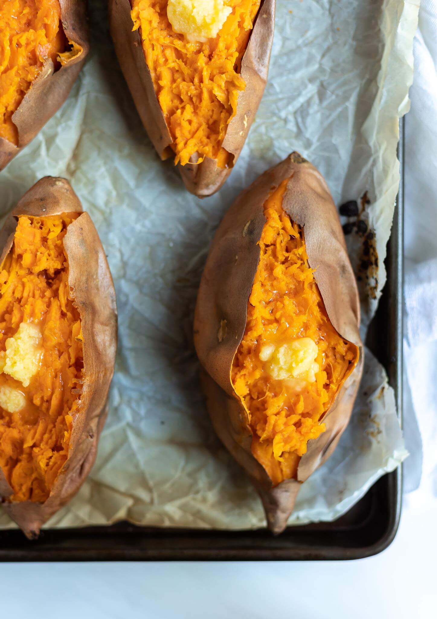 roasted sweet potatoes topped with ghee on parchment paper 