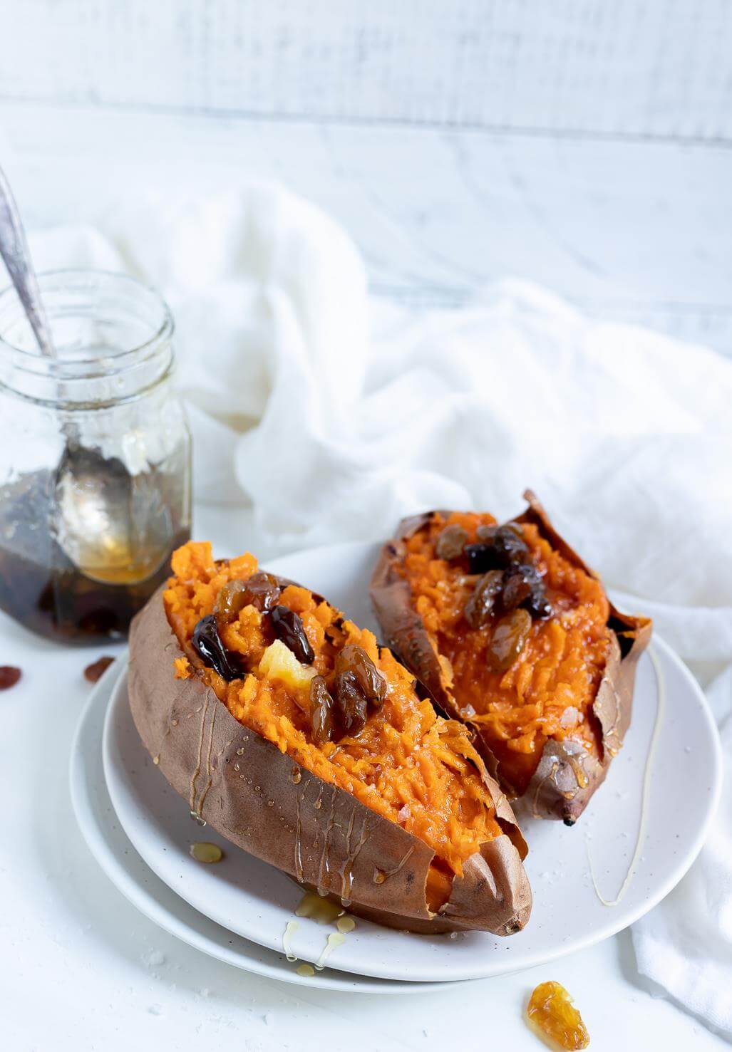 two sweet potatoes topped with honey and raisins on white plate