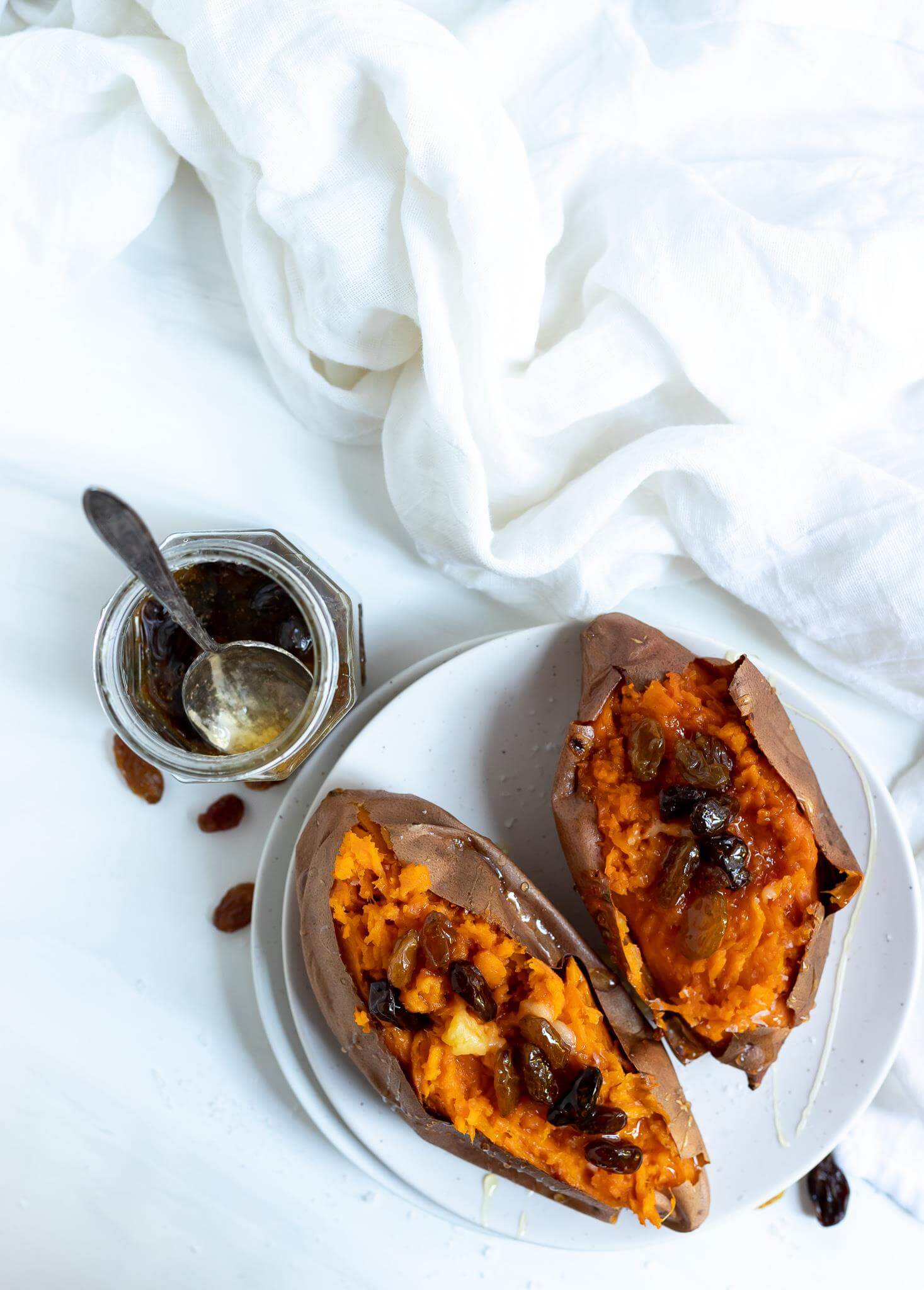 two roasted sweet potatoes on a white plate with jar of honey raisins on the side