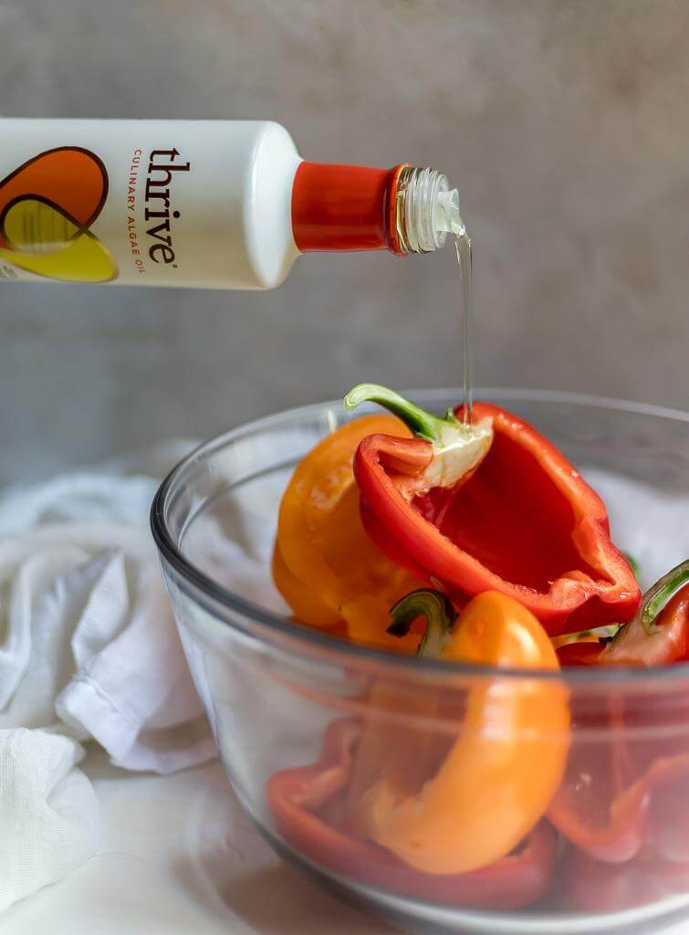 peppers in clear bowl with algae oil being drizzled over the tops