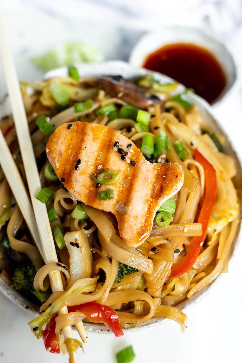 large bowl of vegetables and chinese noodles topped with a fish shaped grilled salmon patty