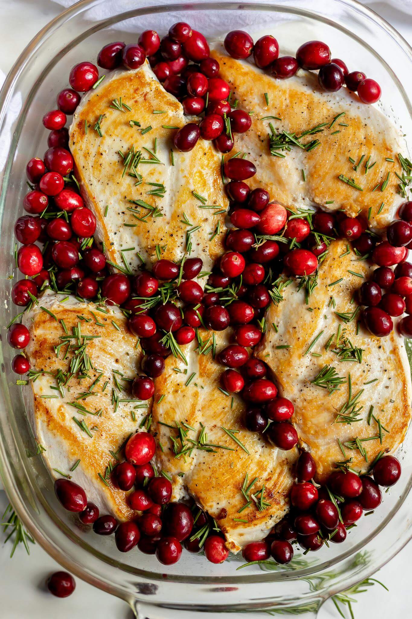 rosemary chicken breasts and fresh red cranberries in glass baking dish