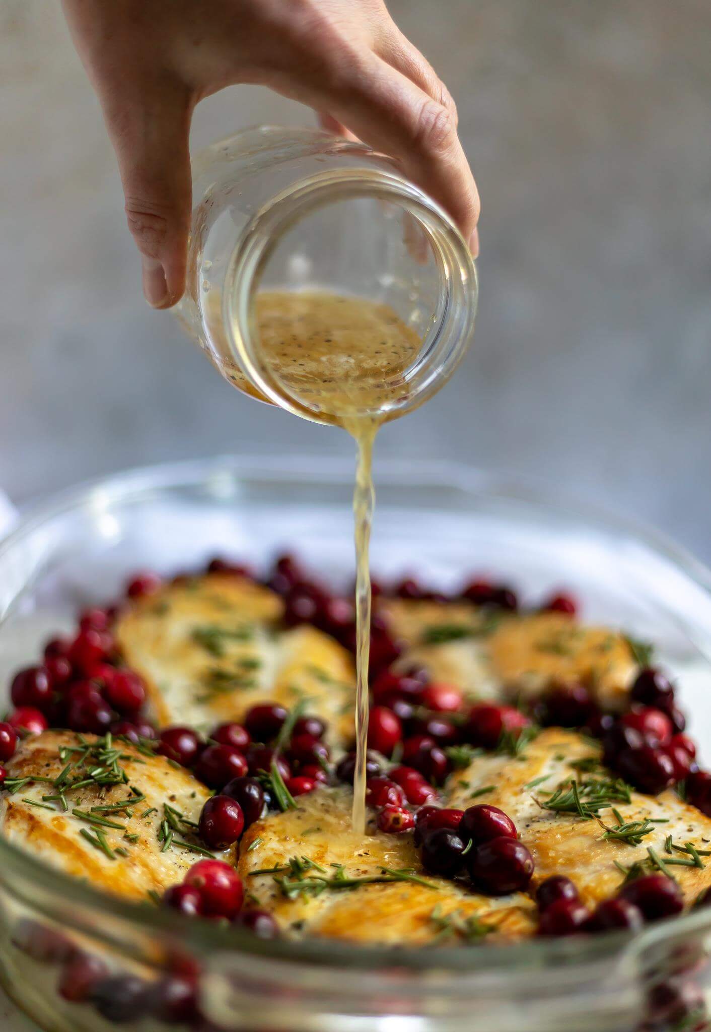 jar of sauce being poured over rosemary chicken in glass baking dish