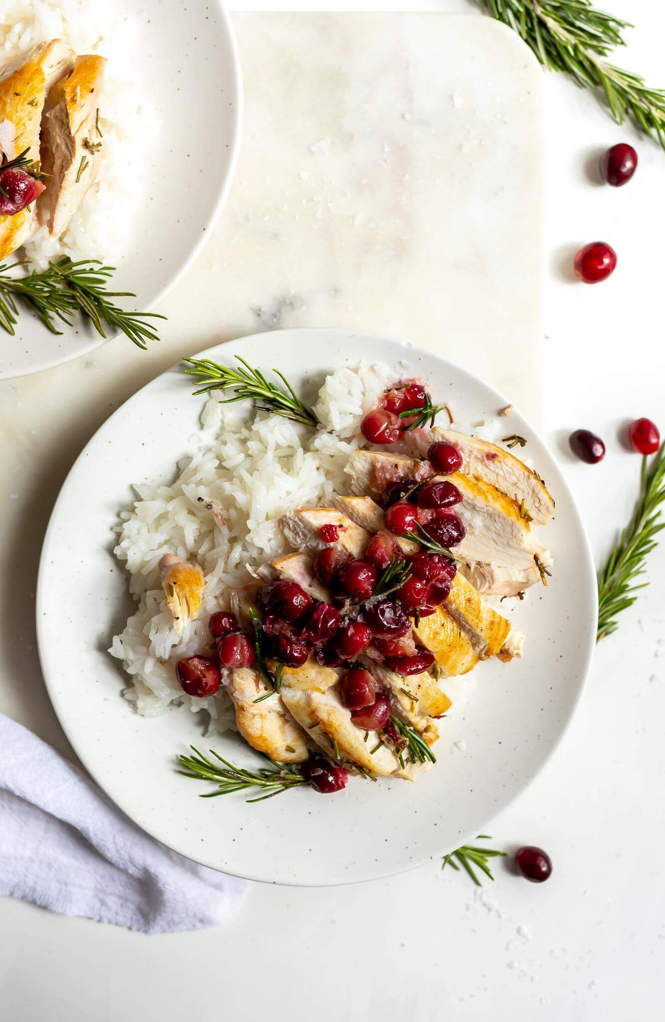 sliced rosemary chicken topped with cranberries served with white rice on a white plate
