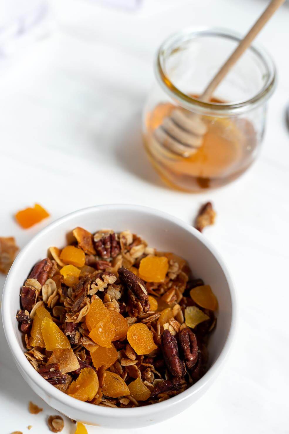 homemade granola in white bowl next to jar of honey