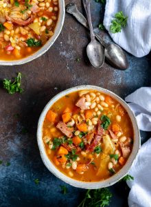two bowls of ham and bean soup and two spoons on the side