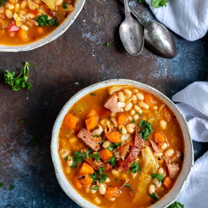 two bowls of ham and bean soup and two spoons on the side
