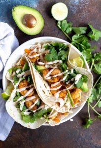 two loaded shrimp tacos with cilantro, lime and avocado on the side