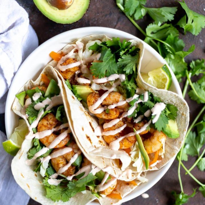 two loaded shrimp tacos with cilantro, lime and avocado on the side