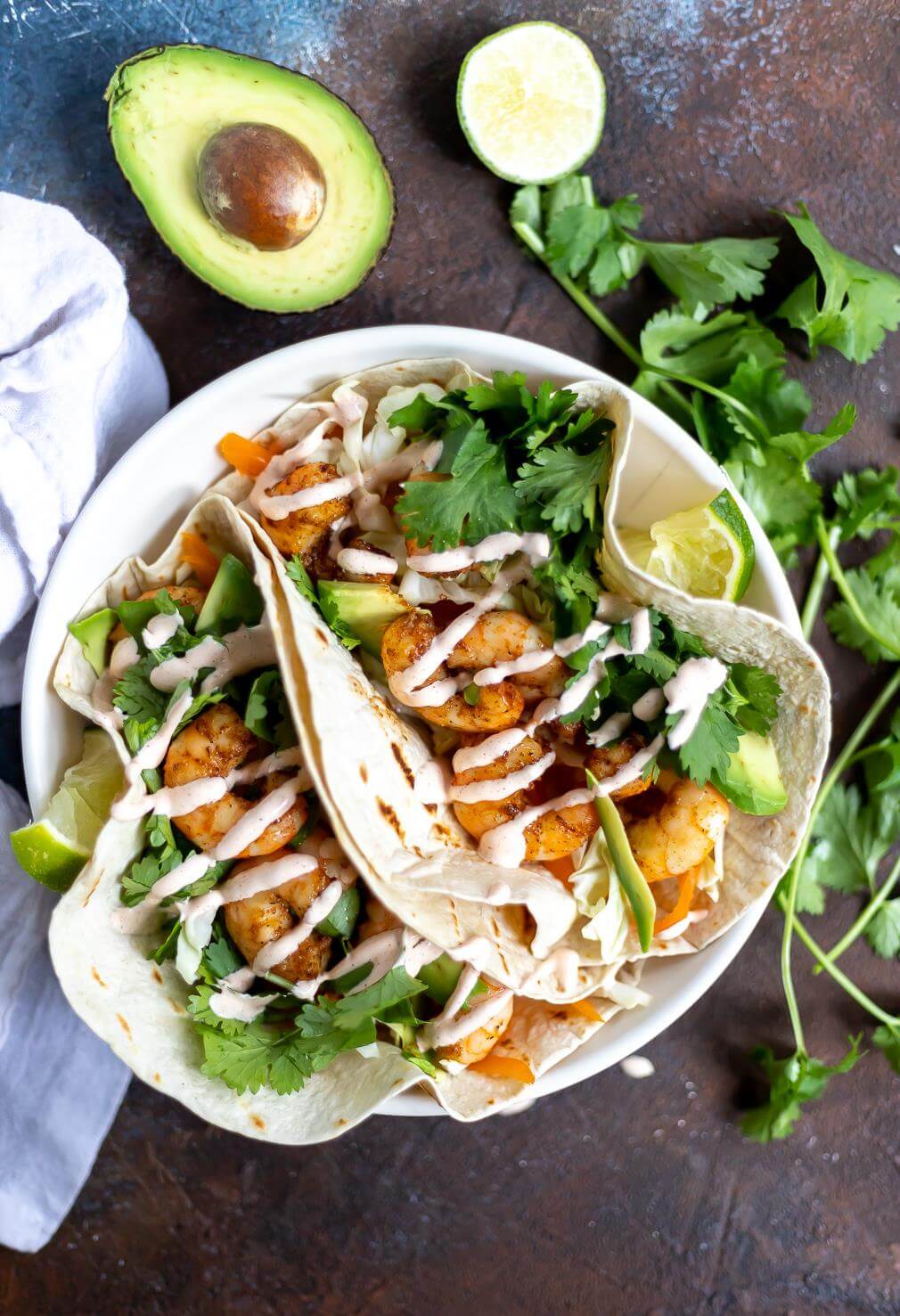 two loaded shrimp tacos with cilantro, lime and avocado on the side