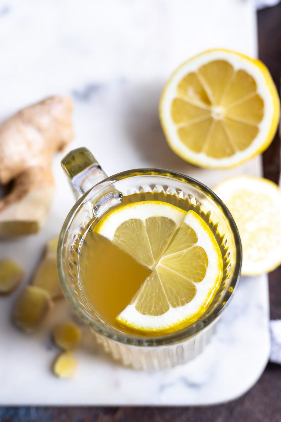 overhead photo of glass mug filled with ginger tea and lemon slices