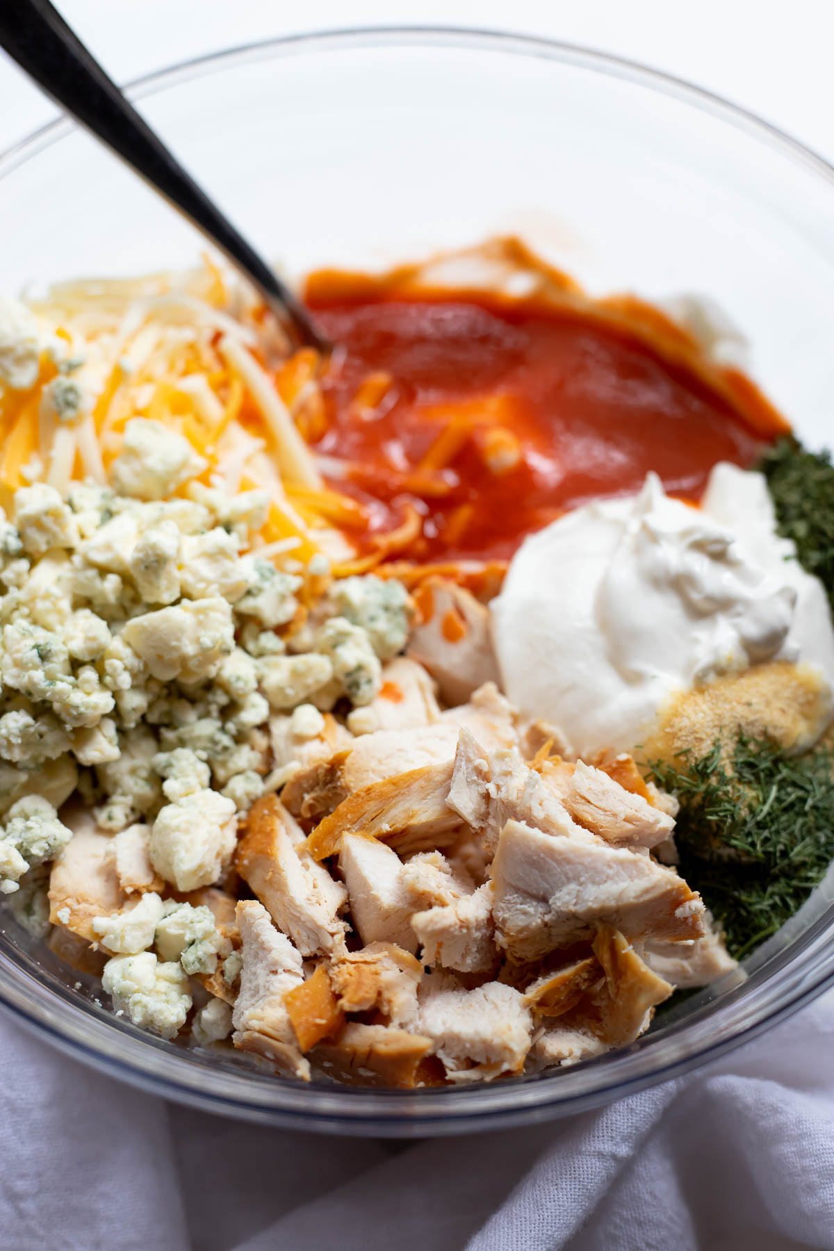 ingredients for buffalo chicken dip in clear glass bowl