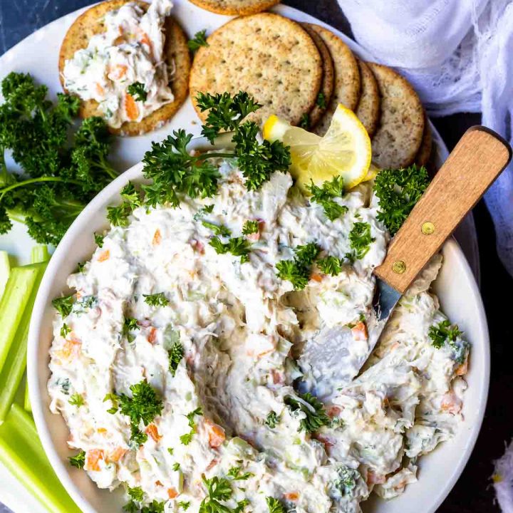cold crab dip in white bowl with metal spreading knife