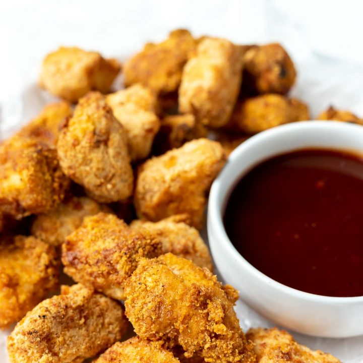 homemade air fryer chicken nuggets on a white plate with barbecue sauce on the side